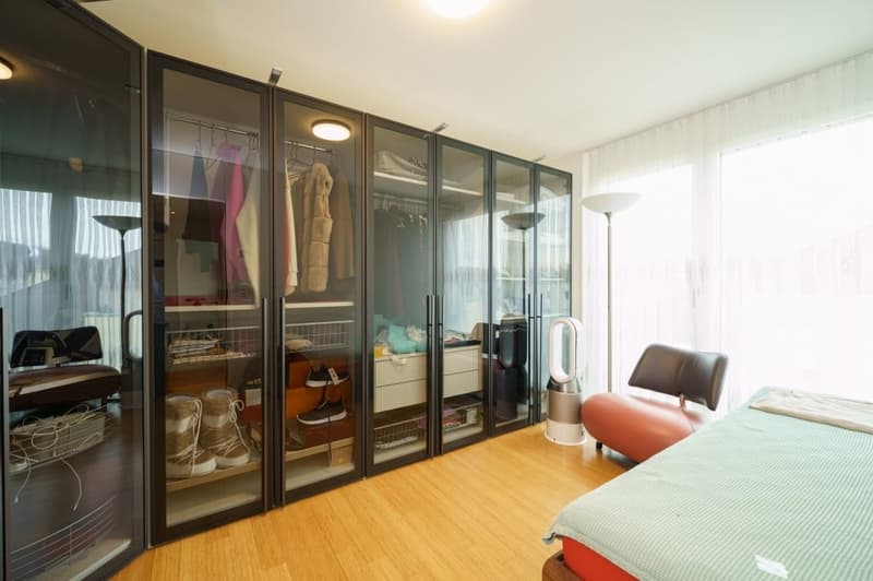 large walk-in closet, wooden floor, bed, chair, lamps, white curtains