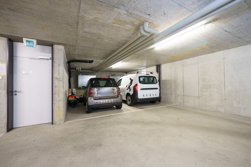 underground parking garage, two cars parked, white walls, concrete floor, white door