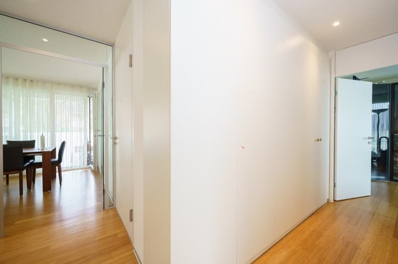 Empty room with white walls, wooden floor, glass doors, and a dining area with a table and chairs.