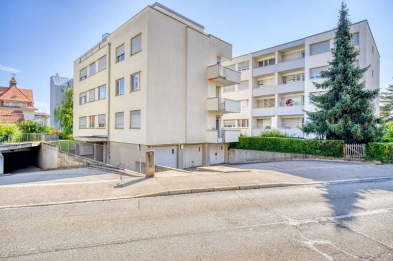 4 story building, beige exterior, multiple windows, balconies, garage, fenced area