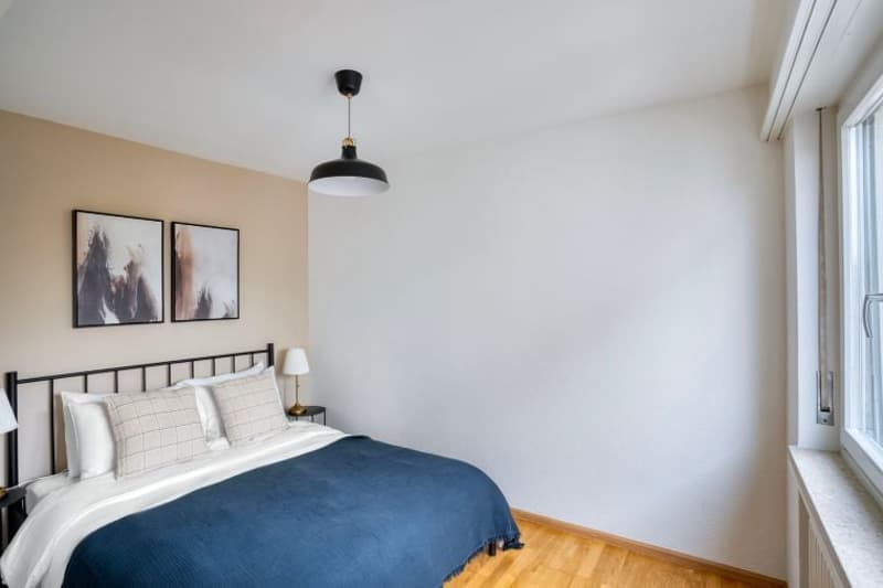 Bedroom with bed, nightstands, lamps, paintings, and wooden floor.