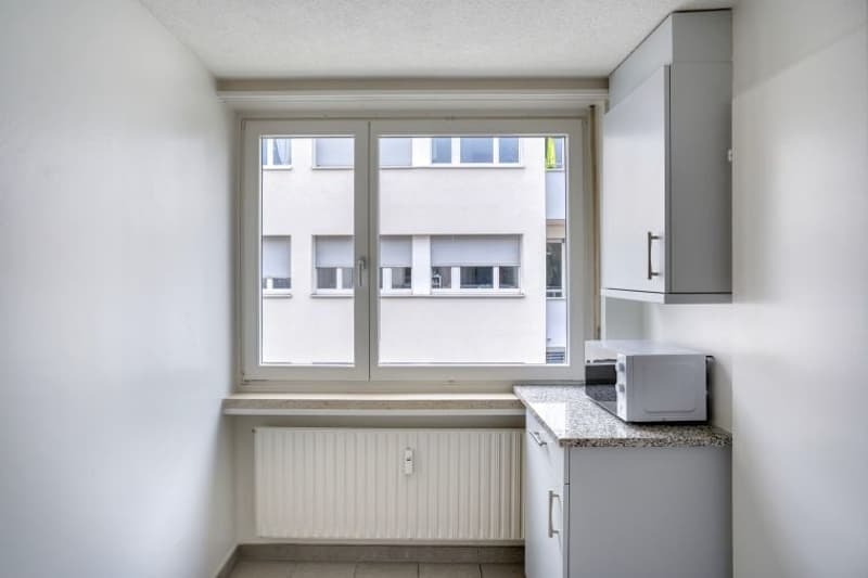 small kitchen with window, microwave, radiator, cabinets