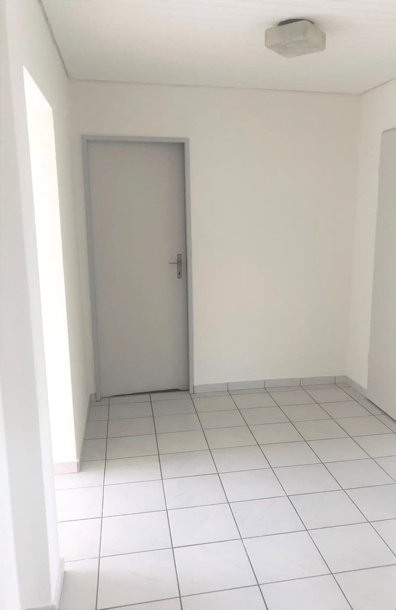 Empty room with white walls, gray tile flooring, and a gray door.