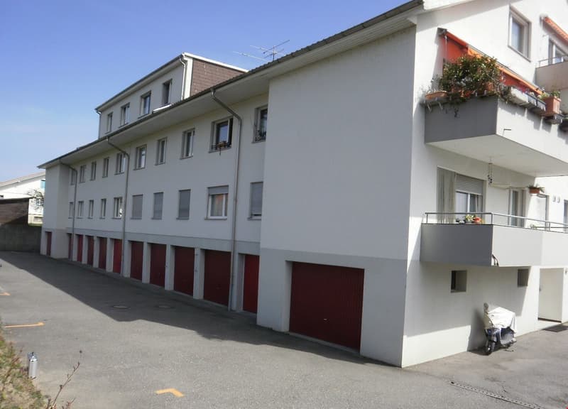 Multi-story apartment building with white exterior walls, red garage doors, and balconies on some units