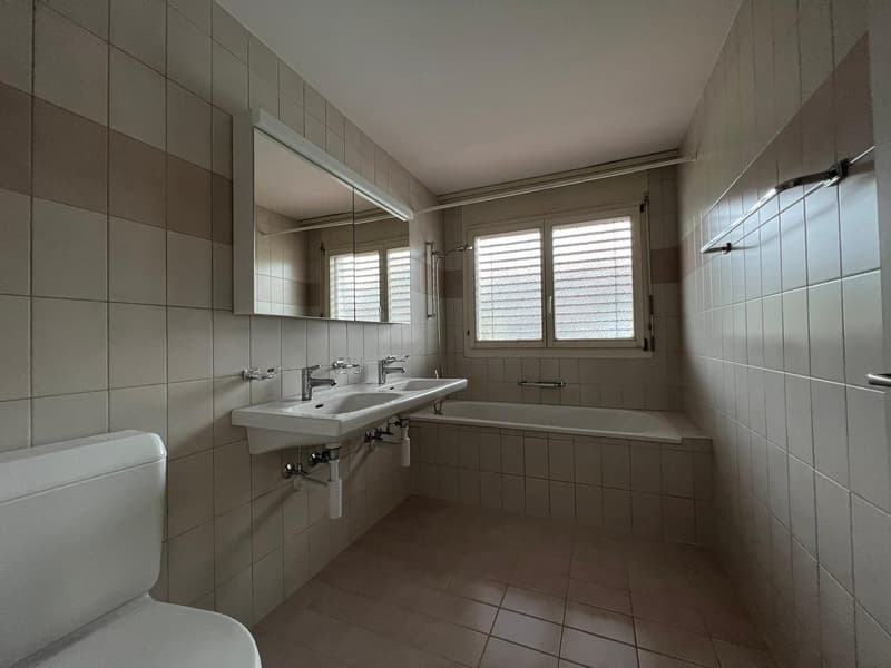 Bathtub, sink with two faucets, toilet, white tiles, mirror, white toilet, modern style