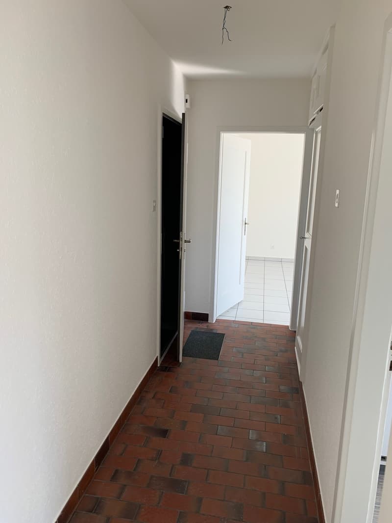 Empty hallway with white walls, red brick floor, two doors, one open