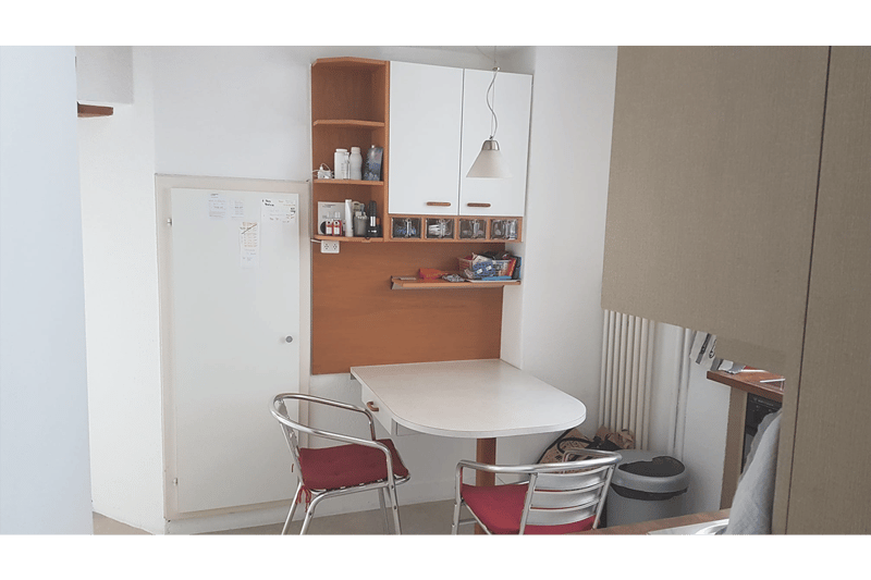 small dining area with table and chairs, open shelf unit with storage and hanging lamp, a door