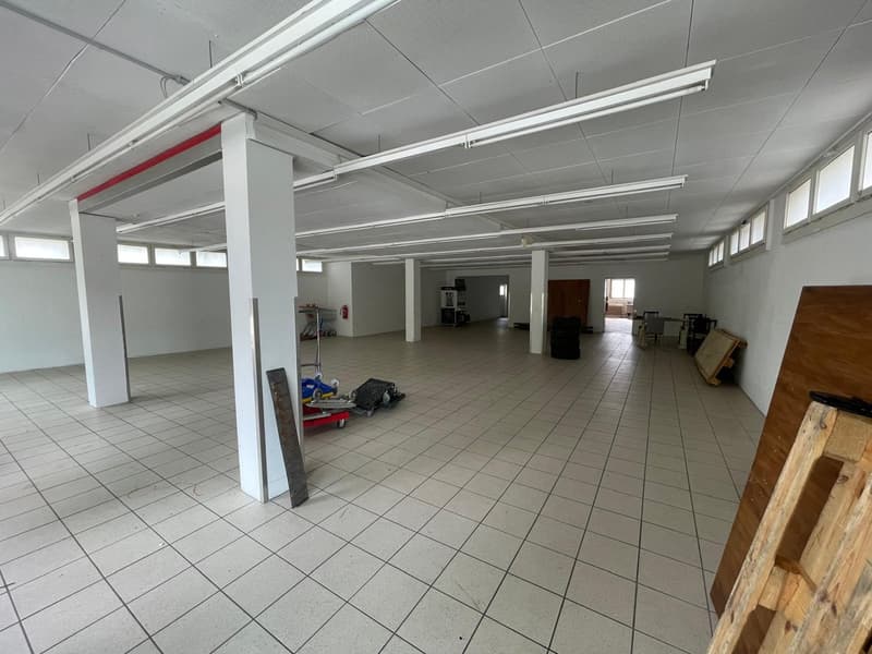 Large open commercial space with tiled flooring, white walls, and suspended ceiling with fluorescent lighting. The space appears to be a warehouse or storage facility, with some equipment and materials visible.