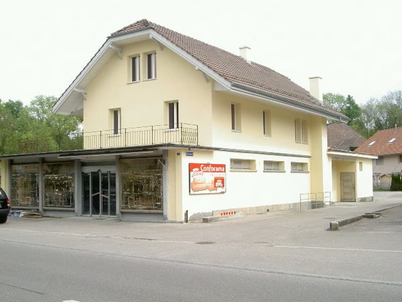 2-story building with a balcony, beige exterior, red tile roof, commercial space on the ground floor, and residential units above