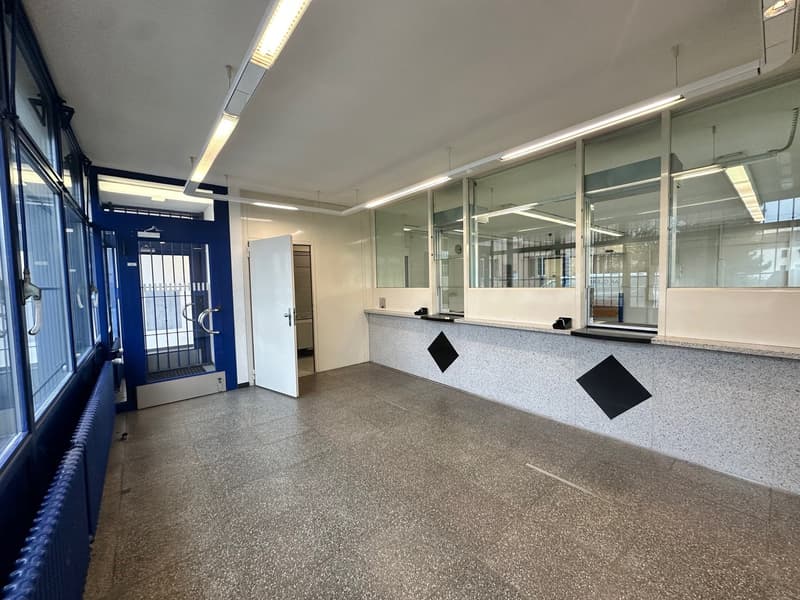 Empty room with white walls, gray floor, blue windows, two black diamond signs on wall, entrance door, and office desk with telephones