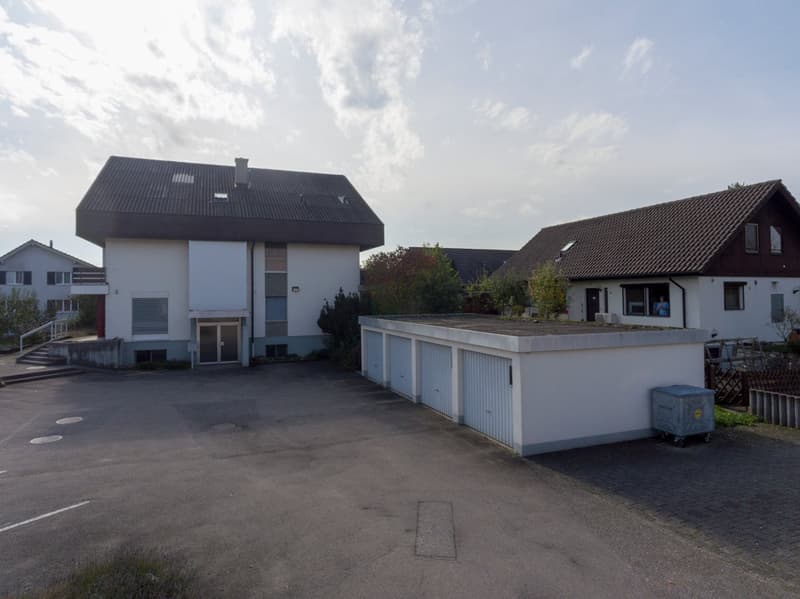 Two houses with garage in the middle. Wide empty space in front.