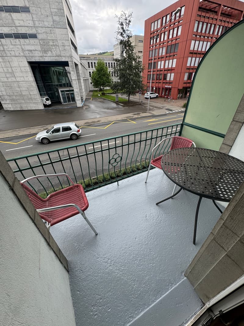 Balcony with metal railing, two red chairs, round table, paved floor, street view