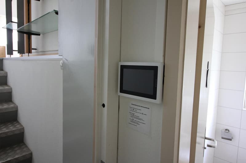 white walls, a monitor mounted on the wall, a white door, a toilet paper holder on the wall