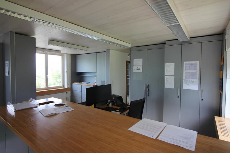 An empty office room with desks, computers, cabinets, and ceiling lights.