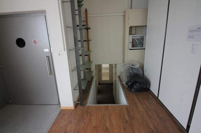 Floor is raised, entrance on the left, stairs leading down, hallway with a door and a microwave