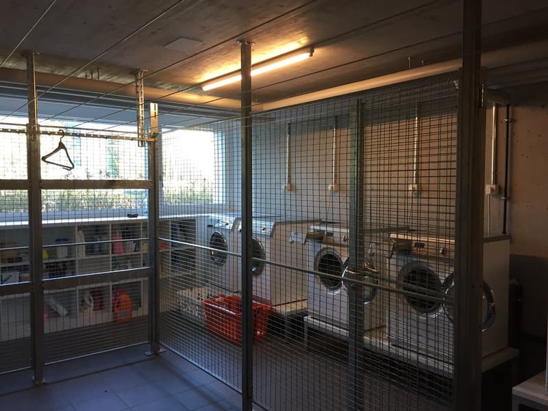 Laundry room with a washing machine, an orange storage basket, a white shelf with items, and metal mesh