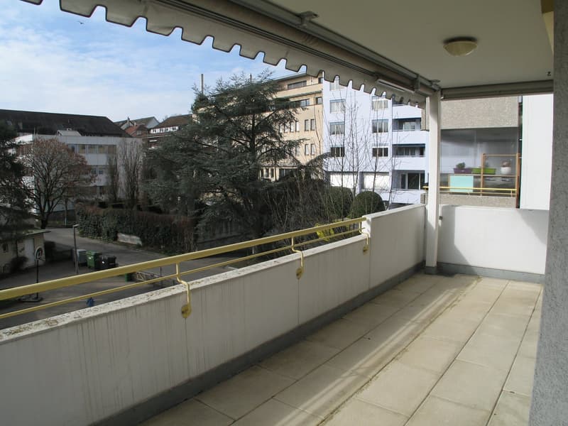 Terrace with railing and tiled floor, distant buildings, trees
