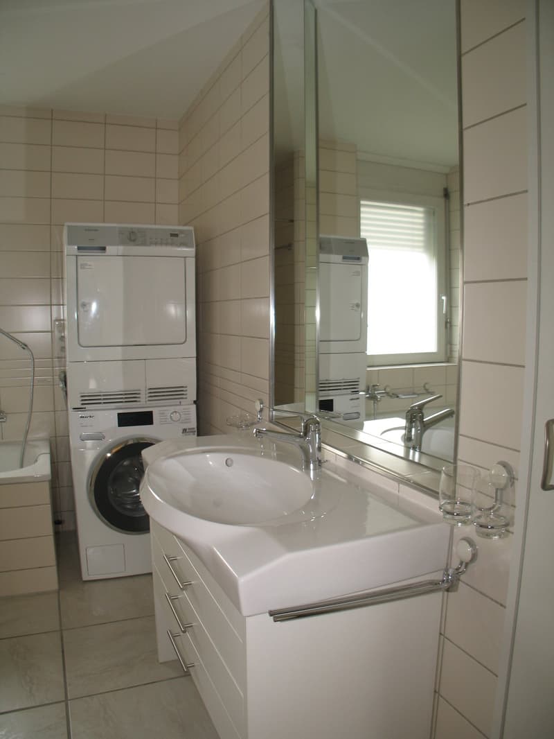 modern bathroom, white sink, white washing machine and dryer, white bathtub, mirror, tiled floor