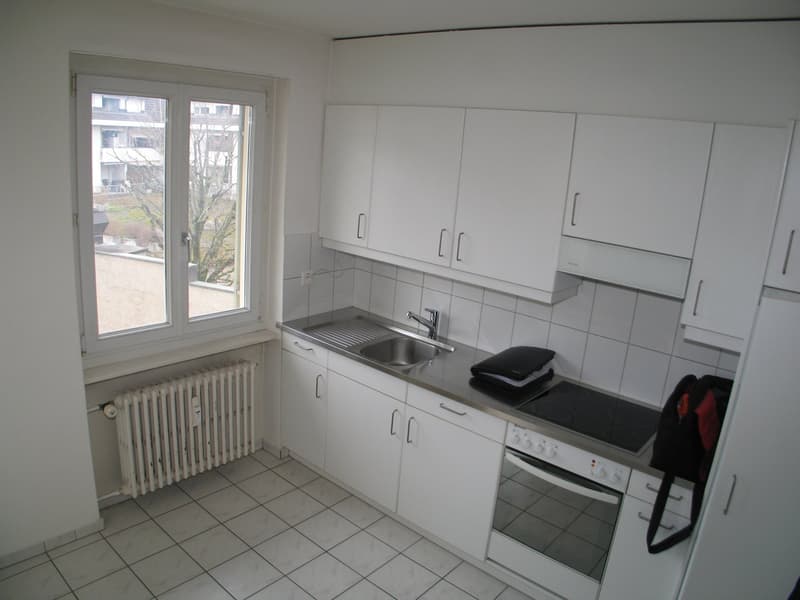 White kitchen with tiled floors and walls, equipped with cabinets, a sink, and a stove.