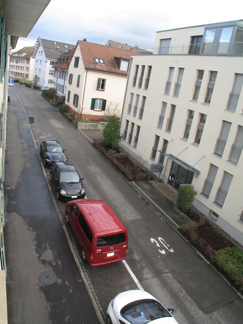 Two storey building, red van parked, grey asphalt, cars parked, road sign, building with multiple windows