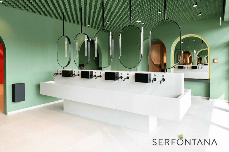 modern bathroom with green walls, white countertop, round mirrors, faucets, and a speaker