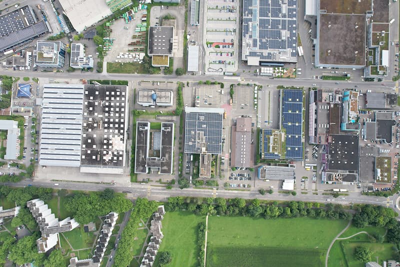 Industrial buildings with parking lots and solar panels on rooftops, roads, and surrounding greenery.