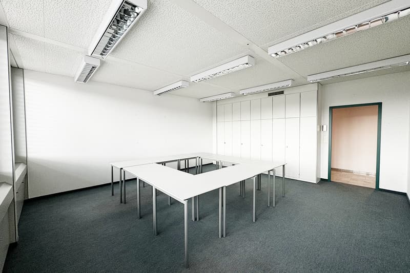 White walls, gray floor, 3 rectangular tables, white cabinets, fluorescent lighting