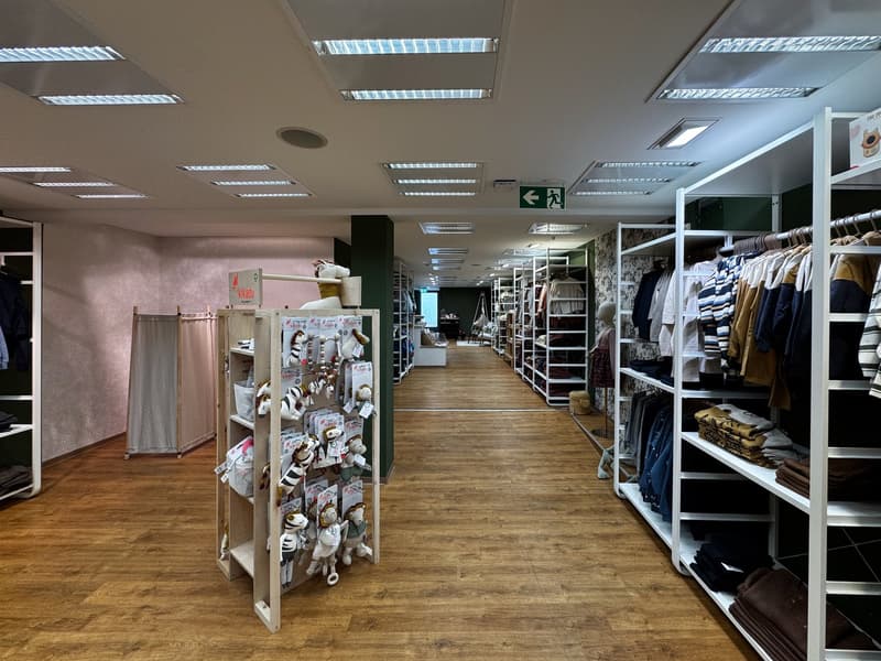 Commercial space, hallway, wooden floor, white shelves, clothing racks, signage, multiple clothing sections