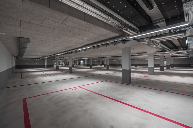 Large indoor parking garage with concrete floors, red parking lines, and exposed ceiling pipes and ductwork.