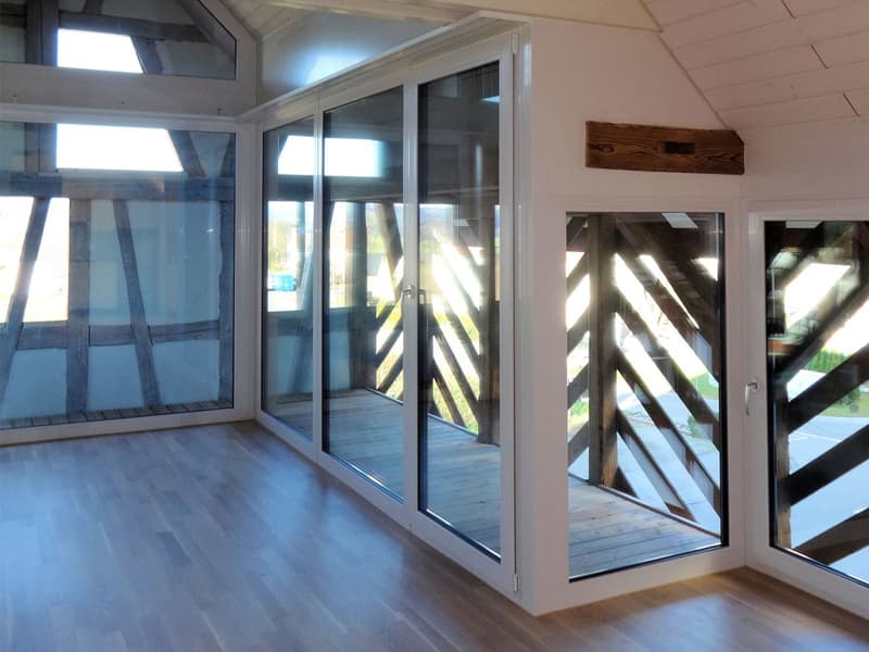 room with sliding glass doors opening to a wooden balcony, wooden beams on the ceiling, wooden flooring