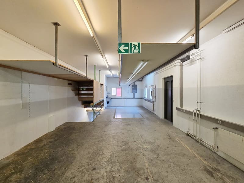 empty hallway, concrete floor, metal beams, storage shelves, fire exit sign