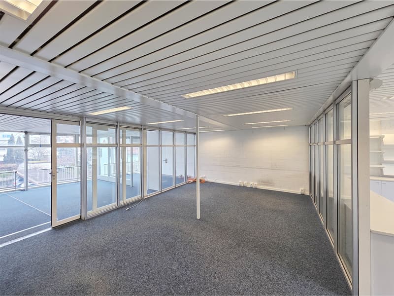 Open space office room with glass doors, glass walls, white walls, white ceiling, gray floor, balcony with railings, outside view