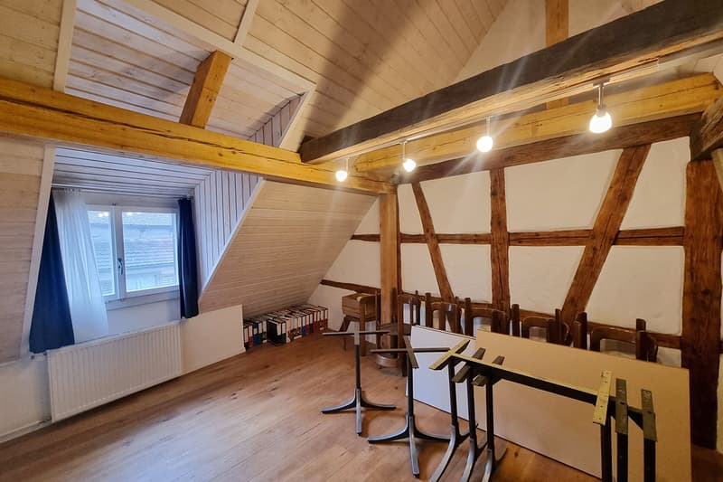 exposed wooden beams, wooden floor, radiator, desk, chairs, books, window with curtains, lamps