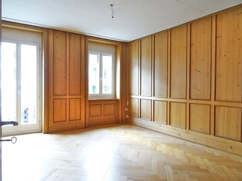 Empty room with wooden walls, wooden floor, two windows, sliding door