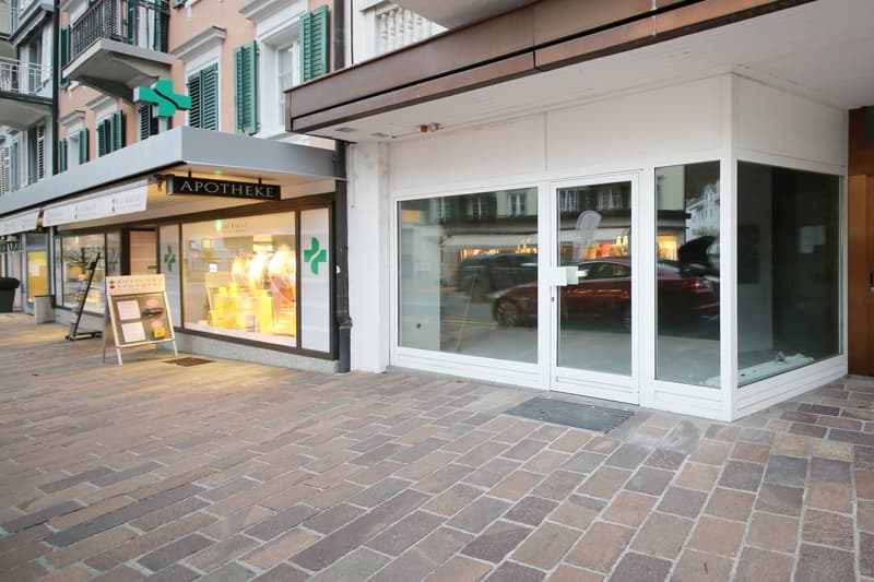 Storefront with glass doors and windows, brick pavement, pharmacy sign, reflection of cars