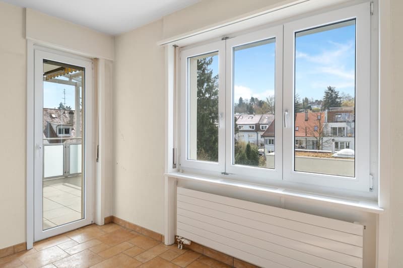 empty room, white walls, brown tiles, sliding glass door, large windows, balcony, radiator, view of trees and buildings