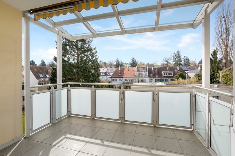 Balcony with glass railings, tiled floor, retractable awning, view of the city