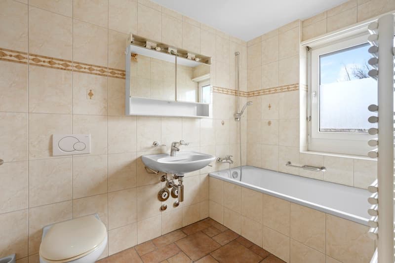 Bathroom with beige tiles, white bathtub, white sink, white toilet, mirror, shower head, window