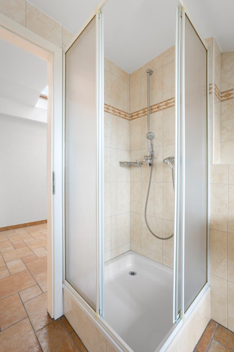 Bathroom with shower, tiled walls, tiled floor, glass door, shower head, drain