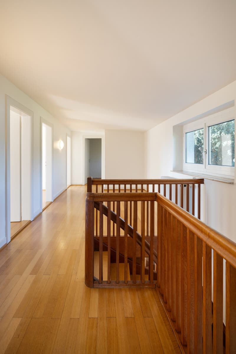 Empty hallway, hardwood floor, wooden railing, doors on both sides, and stairs in the background