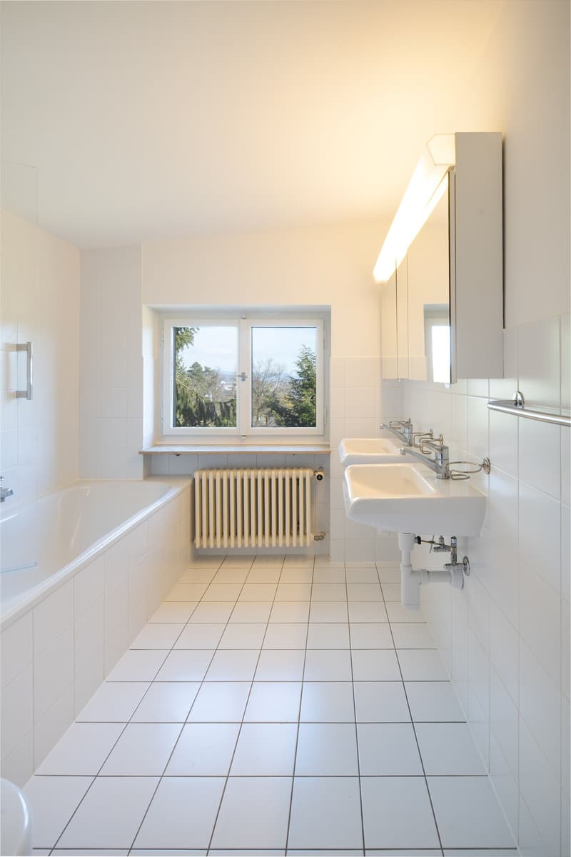 modern clean and minimalist bathroom, white tiles, bathtub, sinks, white toilet, mirror, radiator, window