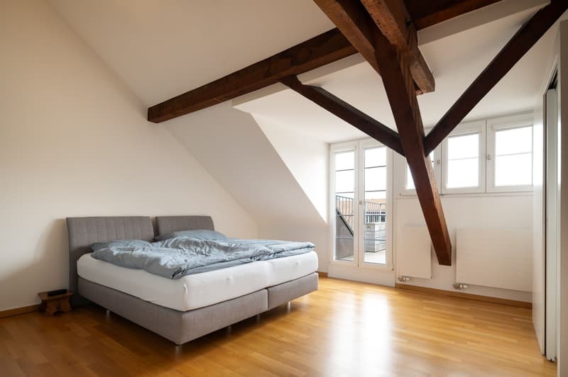 bedroom with wooden floor, bed, wooden beams, windows, balcony