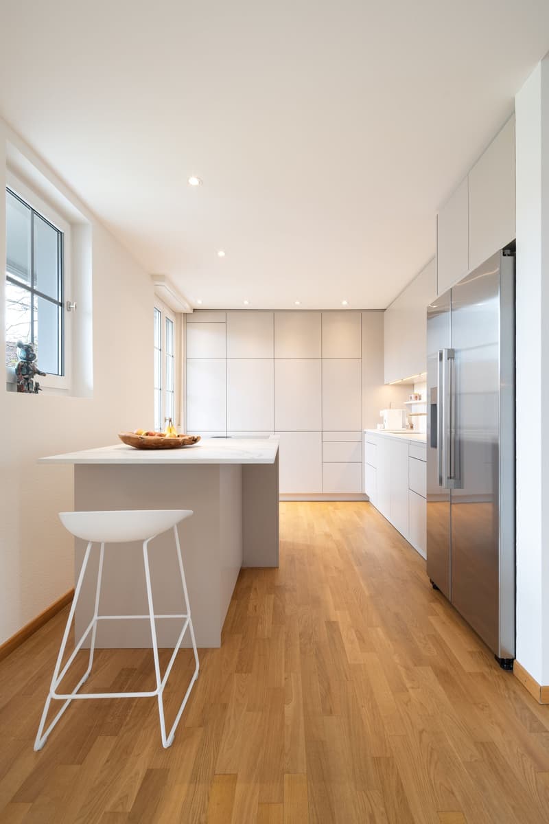 modern kitchen with white cabinets, wooden floor, stainless steel refrigerator, island with fruit bowl, white stool