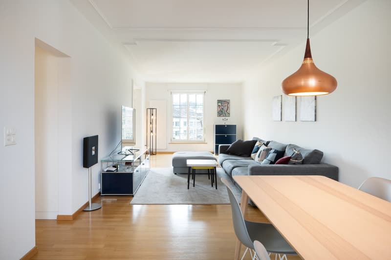 modern living room, gray couch, wooden floor, white walls, TV, entertainment center, dining table, chairs, pendant light