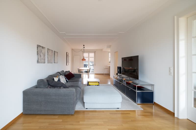 modern living room with gray sofa, wooden floor, white walls, TV, entertainment center, rug, and decorative items