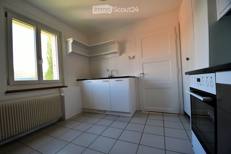 Clean and empty kitchen with white tiles, black and white stove, sink, wooden window and radiator.