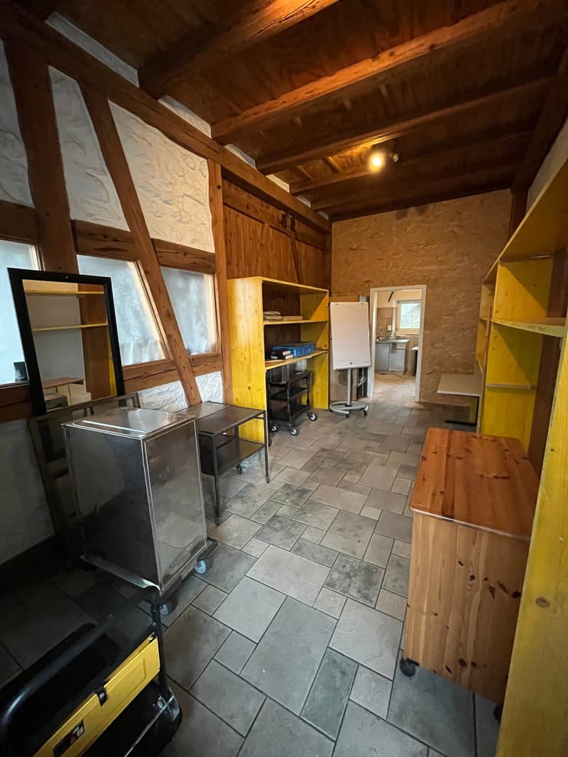 Rustic kitchen with wooden beams, stone walls, tile flooring, shelving units, appliances including a refrigerator and washing machine, and various storage and cooking equipment