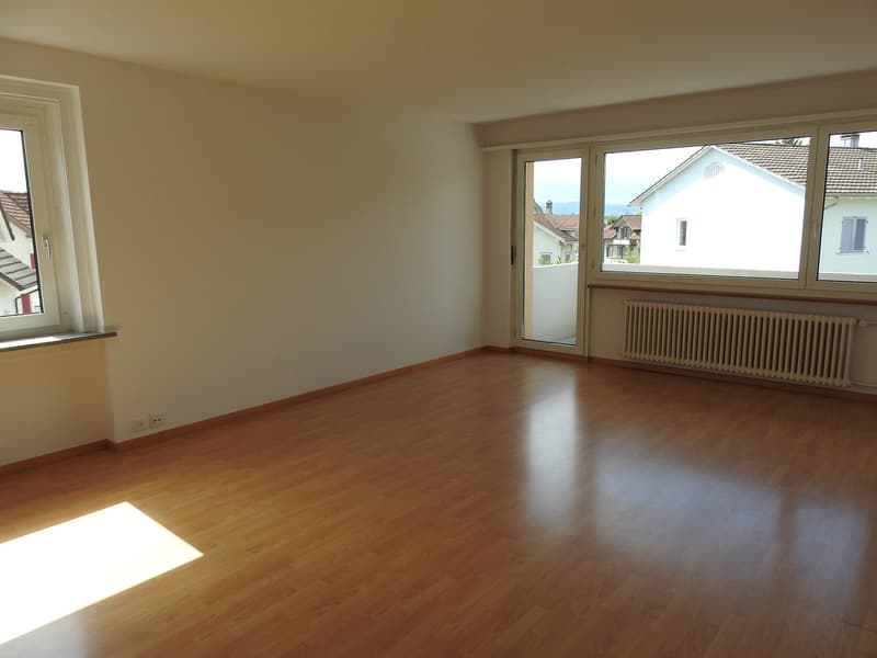 Empty room, hardwood floor, white walls, sliding glass door to balcony, radiators, double windows, power outlets