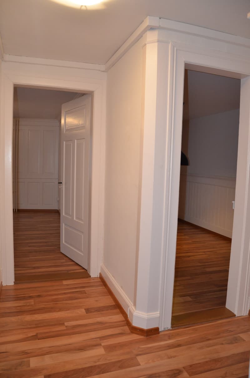 Empty room with wooden floor, white walls, two doors, and a ceiling light