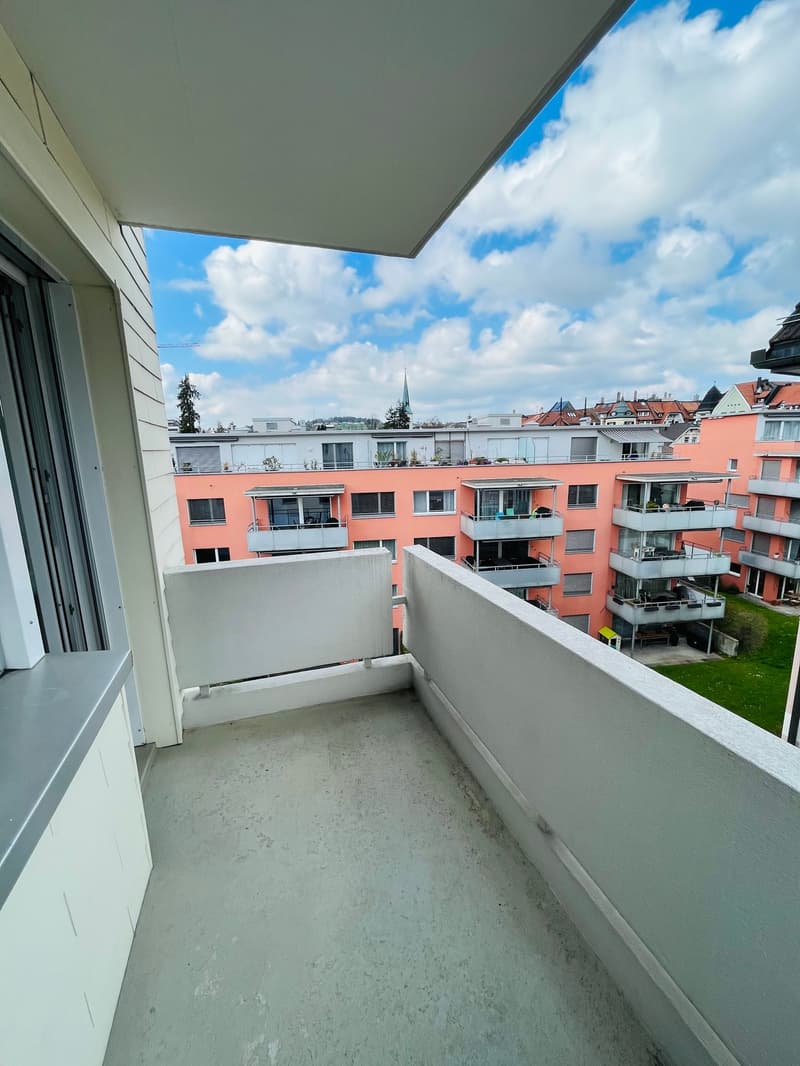 Large balcony with white railings, concrete flooring, gray stonework, city view